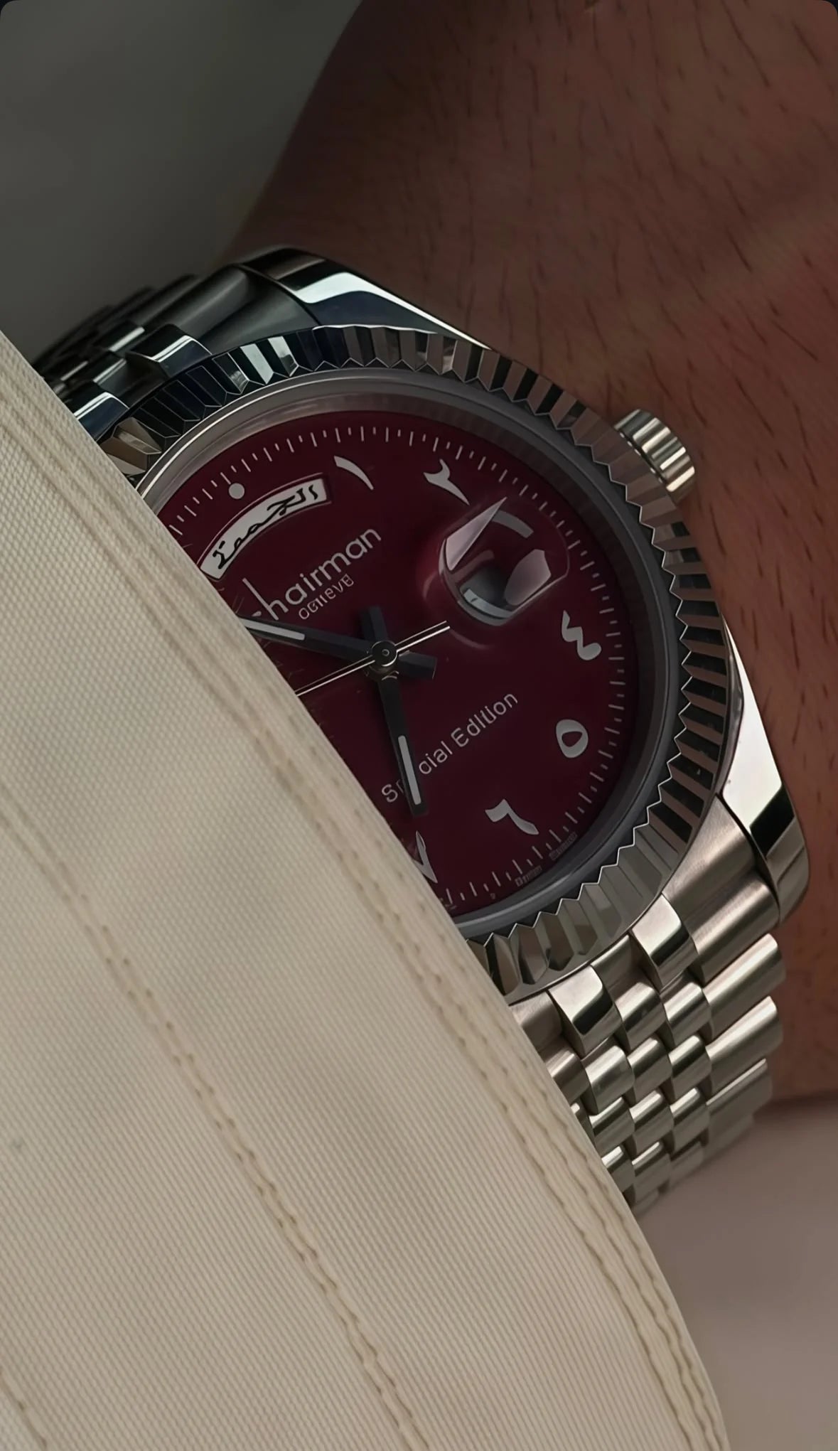 Watch with a red face and silver case on a wrist against a neutral
background available on Salam Luxury UAE