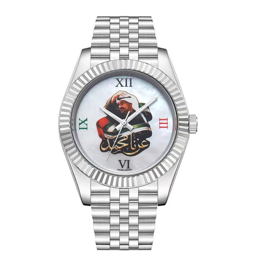 A silver stainless steel wristwatch with a fluted bezel, a silver link bracelet, and a white dial featuring a central graphic of a bearded man in a turban and red bag, with Arabic calligraphy and Roman numeral hour markers. Salam Luxury