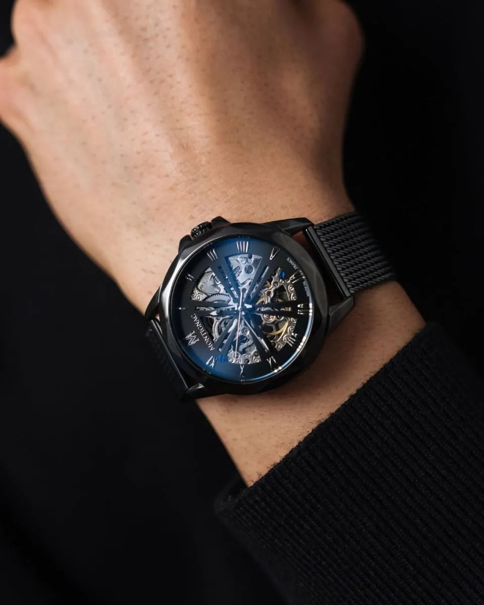 Black wristwatch with a blue face on a person's wrist against a dark background