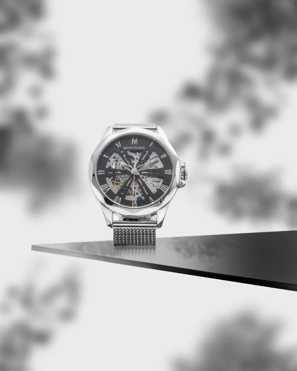 Silver watch with a detailed face on a reflective surface, blurred natural background