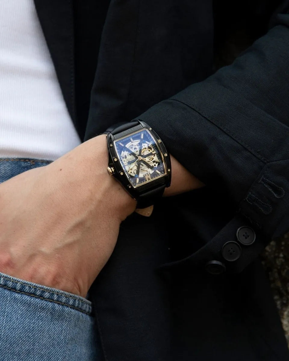 Person wearing a black wristwatch with a detailed face, dressed in a dark coat and jeans.