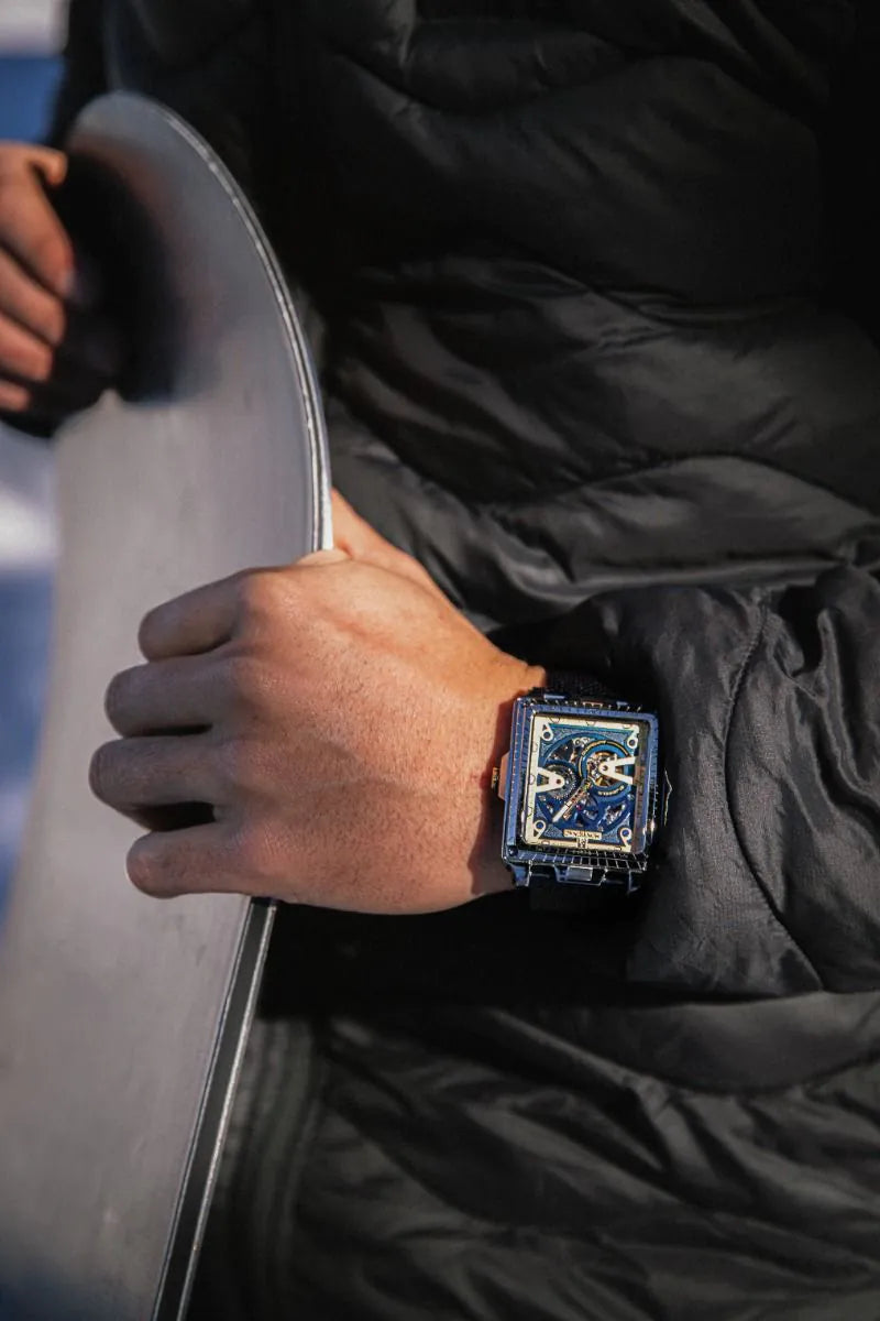 Person wearing a black jacket holding a skateboard with a close-up of a watch on their wrist.
Salam Luxury