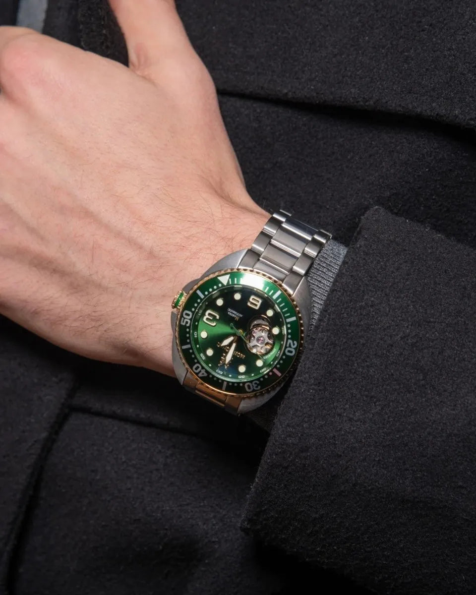 Green wristwatch with silver strap on a person's wrist against a black background