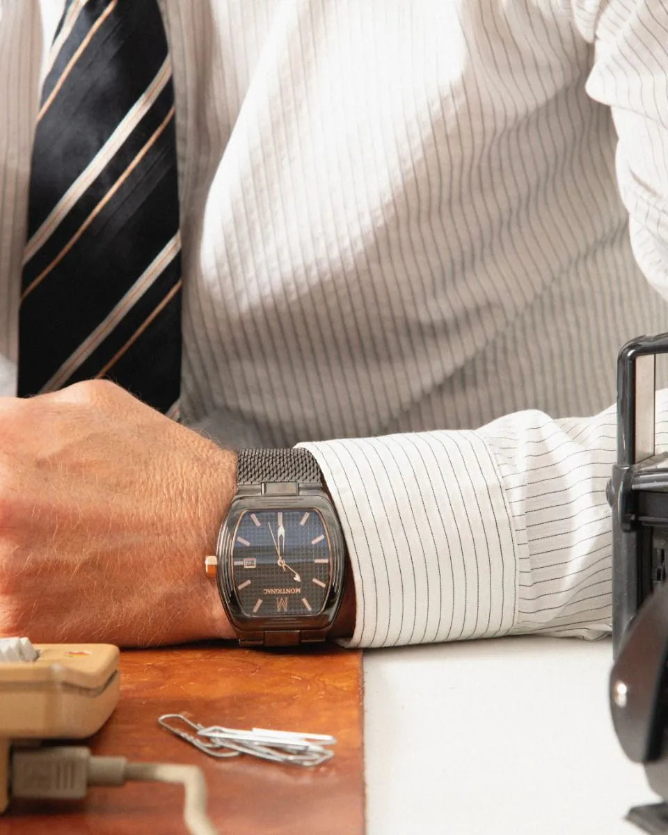 Person wearing a watch with a striped shirt and tie, sitting at a desk.