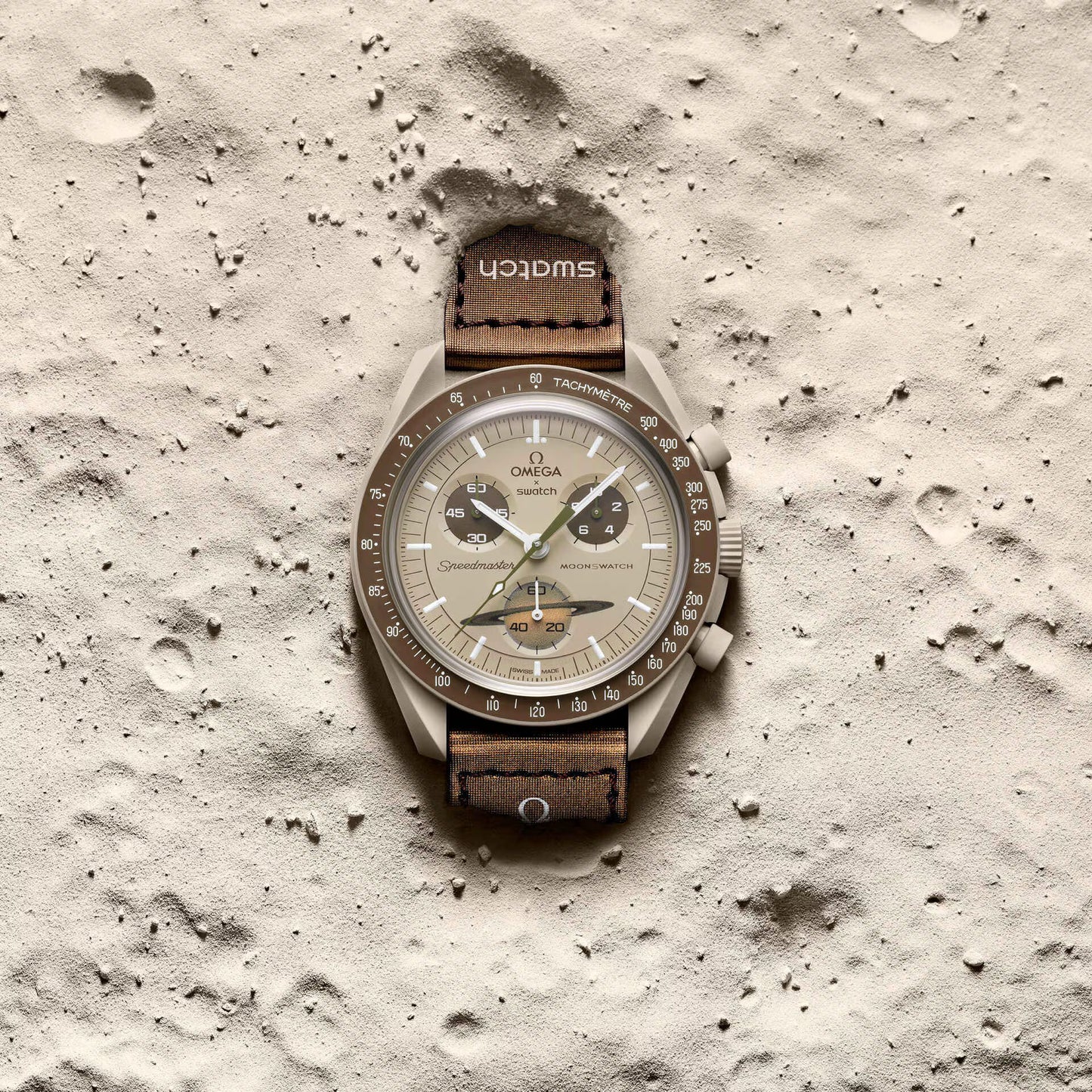 Omega x Swatch MoonSwatch Mission to Saturn SO33T100 beige watch lying on sandy surface
