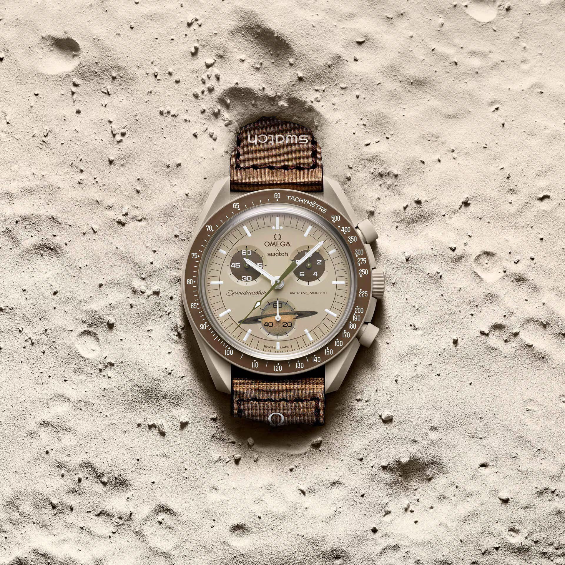 Omega x Swatch MoonSwatch Mission to Saturn SO33T100 beige watch lying on sandy surface