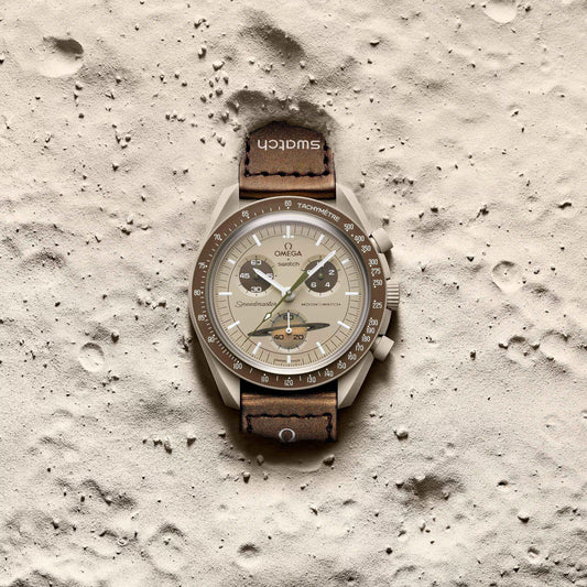 Omega x Swatch MoonSwatch Mission to Saturn SO33T100 beige watch lying on sandy surface